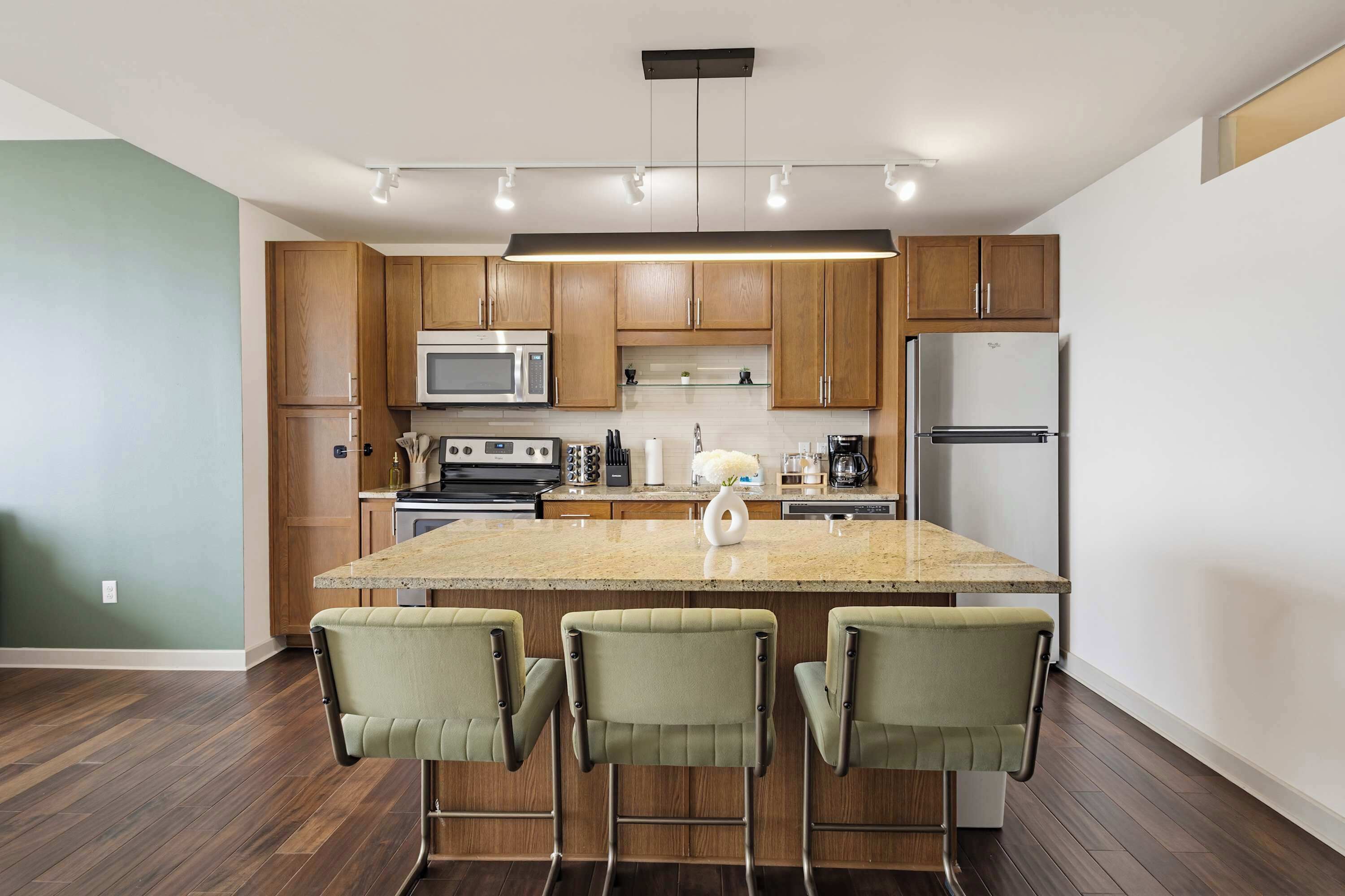Une cuisine moderne avec des meubles en bois, un îlot central, des tabourets de bar et des appareils électroménagers en acier inoxydable.