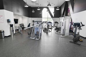 Et fitnessrum med diverse træningsmaskiner, kaffestation og skraldespand.
