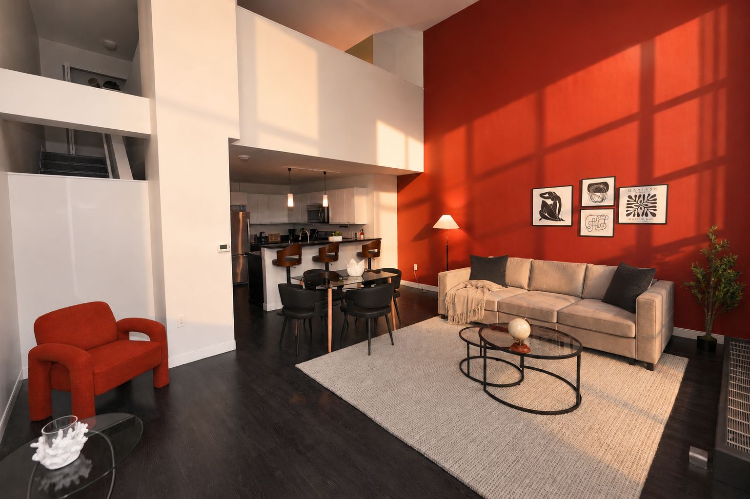 A modern living room with a sofa, coffee table, and red chair. A kitchen is visible in the background.