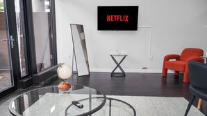 Un soggiorno moderno con un tavolino in vetro, un mappamondo, un telecomando, una poltrona rossa, una sedia nera, una TV che mostra 'NETFLIX' e un piccolo tavolino.