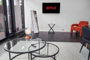 En moderne stue med et glasbord, en globus, en fjernbetjening, en rød lænestol, en sort stol, et fjernsyn der viser 'NETFLIX' og et lille sofabord.