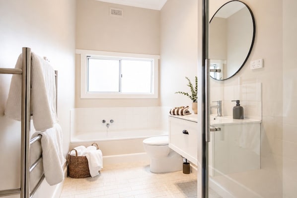 A modern bathroom with a bathtub, toilet, and a large mirror. - Heritage 3-Bed Home | Walk to Sovereign Hill & CBD (Golden Point)