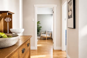 A hallway with a wooden dresser, a white chair, and a plant. - Heritage 3-Bed Home | Walk to Sovereign Hill & CBD (Golden Point)