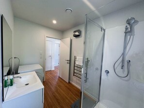 Ein modernes Badezimmer mit Duschkabine aus Glas, einem weißen Waschbecken und einem Spiegel.