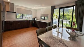 A modern kitchen with dark wood cabinets, a marble countertop, and a dining area with a glass table and chairs.