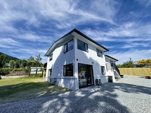 Une maison moderne à deux étages, avec une allée en gravier, de grandes fenêtres et une clôture en bois à l’arrière.