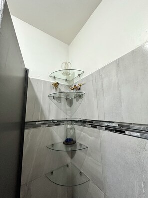 Une salle de bain moderne avec une étagÚre en verre, un dÎme en verre et un mur recouvert de carreaux.
