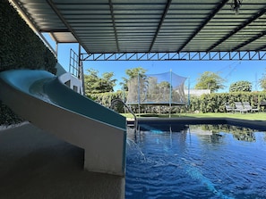 Une piscine avec un toboggan, un trampoline et un espace abrité.