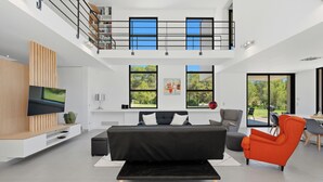 A modern living room with a black sofa, a red armchair, a flat-screen TV, and a balcony with a railing. - Villa Stark - Pool - Gym - Pintball/Arcade/Babyfoot (Saint-Gély-du-Fesc)