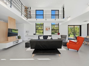 Ein modernes Wohnzimmer mit einer schwarzen Couch, einem roten Sessel, einem Flachbildfernseher und einem Balkon mit Geländer.