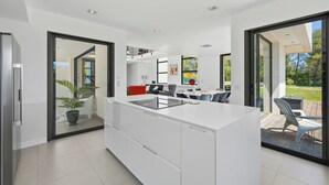 A modern kitchen with a central island, sliding glass doors to a patio, and a view of the outdoors. - Villa Stark - Pool - Gym - Pintball/Arcade/Babyfoot (Saint-Gély-du-Fesc)