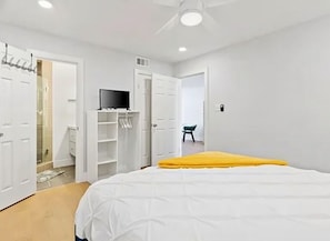 Ein Schlafzimmer mit einem Bett, einem Fernseher, einem Kleiderschrank und einem durchgegangenen Tür sichtbaren Badezimmer.