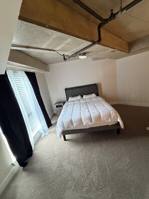 A bedroom with a bed, a window with blinds, a nightstand, and a ceiling with exposed pipes. - Luxury Loft in Midtown Atlanta (Atlanta)