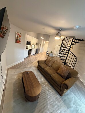 A modern living room with a sofa, a wooden coffee table, a kitchen in the background, and a spiral staircase. - Luxury Loft in Midtown Atlanta (Atlanta)