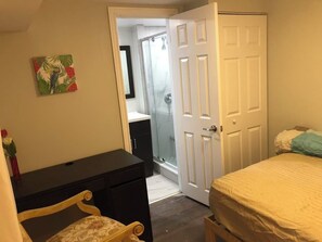 Une chambre à coucher comprenant un lit, une commode, une chaise, une porte et un espace douche.