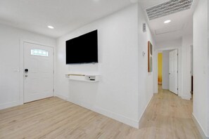 Ein Zimmer mit einem an der Wand befestigten Flachbildfernseher, einer weißen Tür und einem Flur, der zu einem anderen Zimmer führt.