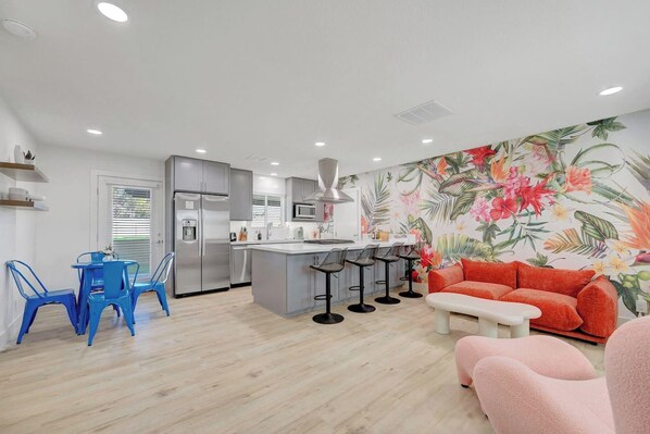 A modern kitchen with a central island, bar stools, and a vibrant floral wall mural. - Iroquois Getaway (North Las Vegas)