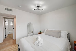 Ein Schlafzimmer mit einem Bett, einem Nachttisch, einem Spiegel und einer Deckenleuchte.