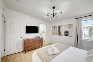 A bedroom with a bed, a dresser, a flat-screen TV, abstract wall art, and a window with curtains. - Hickey Getaway Pool, BBQ & Modern Comfort! (North Las Vegas)