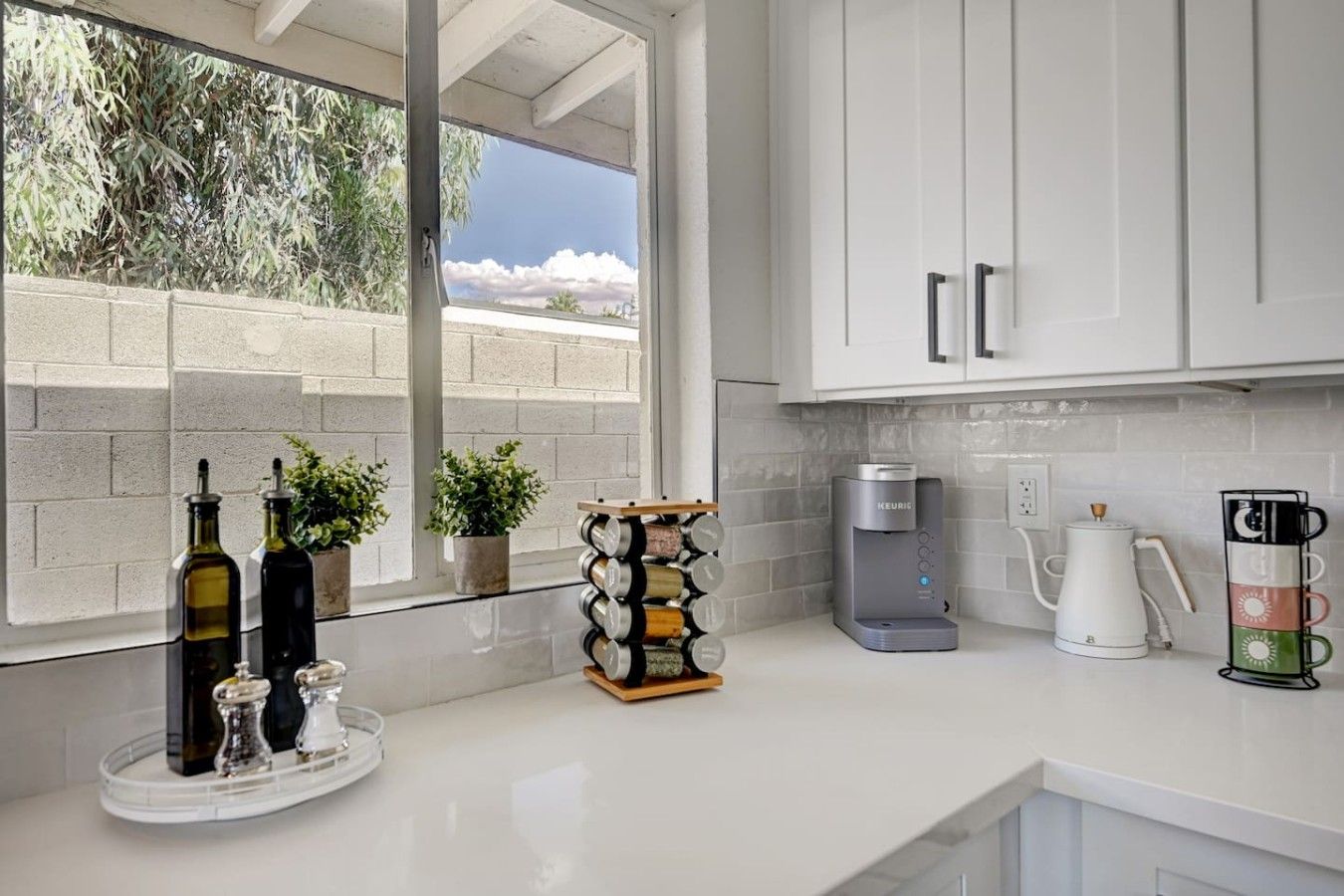A modern kitchen with white cabinets, a coffee maker, a kettle, and a wine rack with bottles.