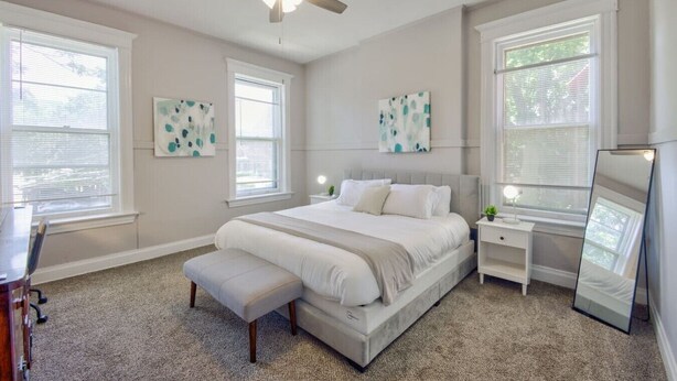 Ein Schlafzimmer mit einem Bett, Nachttischen, einer Bank, einem Deckenventilator und Kunstwerken an den Wänden.