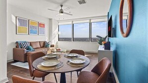 Uma sala de estar moderna com área de jantar, ventilador de teto, janelas amplas e obras de arte na parede.