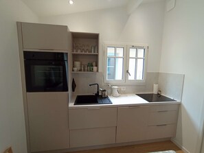 A compact kitchen with a built-in oven, a sink, and a window with blinds. - 250 – Cozy house with enclosed garden, close to the center, everything within walking distance (SOULAC SUR MER)