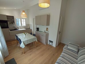A compact kitchen with a dining table, a coffee machine, and a sofa in a living area. - 250 – Cozy house with enclosed garden, close to the center, everything within walking distance (SOULAC SUR MER)