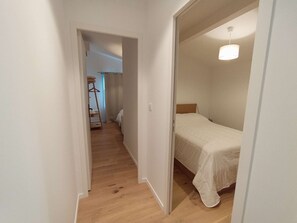 A narrow hallway leading to a bedroom with a bed and a hanging light fixture. - 250 – Cozy house with enclosed garden, close to the center, everything within walking distance (SOULAC SUR MER)