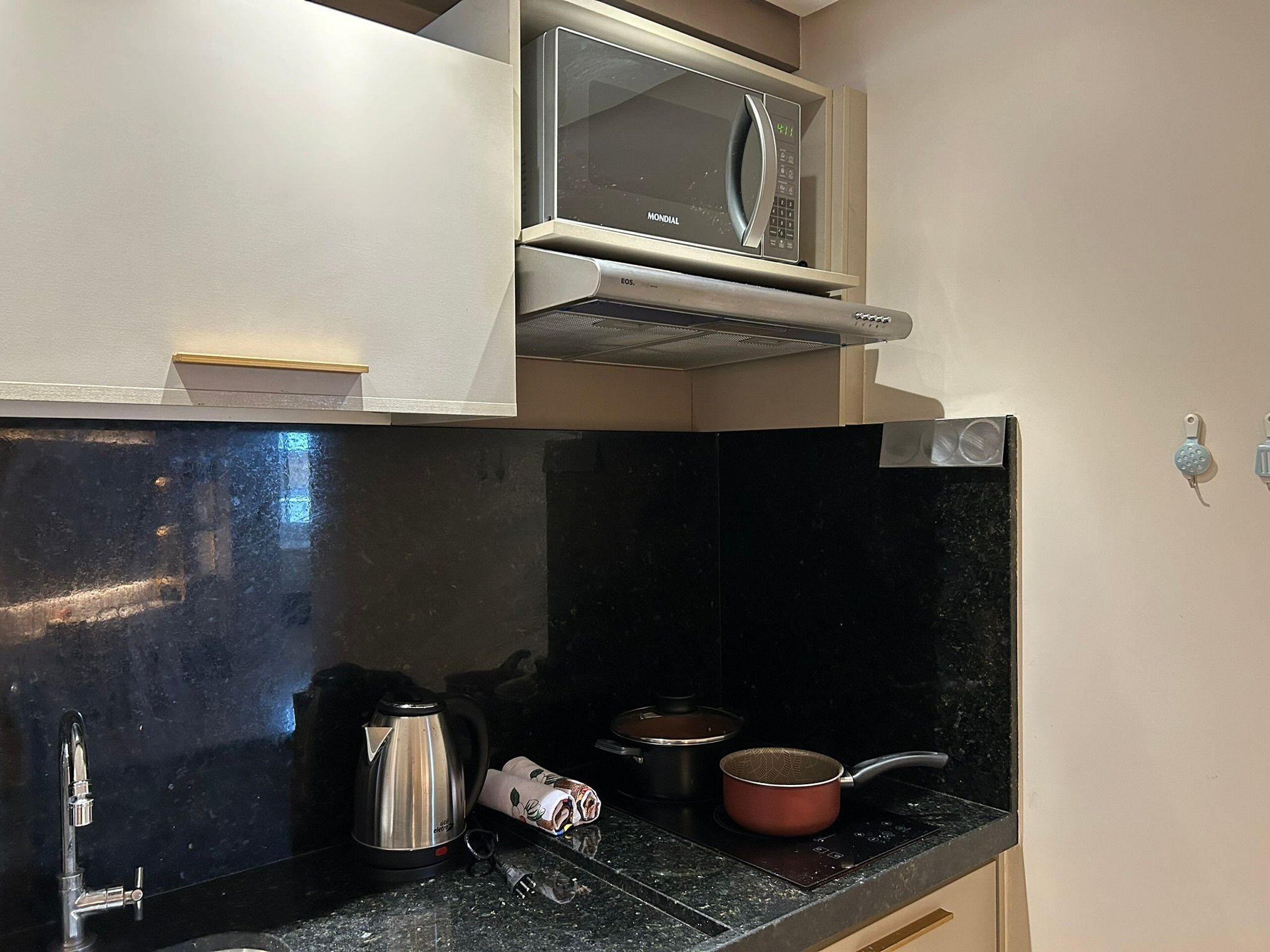 A kitchen with a microwave, kettle, and pots on the counter.
