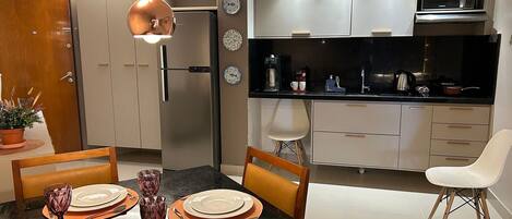 Cozinha moderna com micro-ondas, máquina de café e armários. Há uma mesa de jantar posta com pratos e copos.