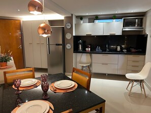 Eine moderne Küche mit Mikrowelle, Kaffeemaschine und Schränken. Ein Esstisch ist mit Tellern und Gläsern gedeckt.
