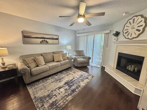 Ein Wohnzimmer mit einer Couch, einem Sessel, einem Kamin und einem Deckenventilator.