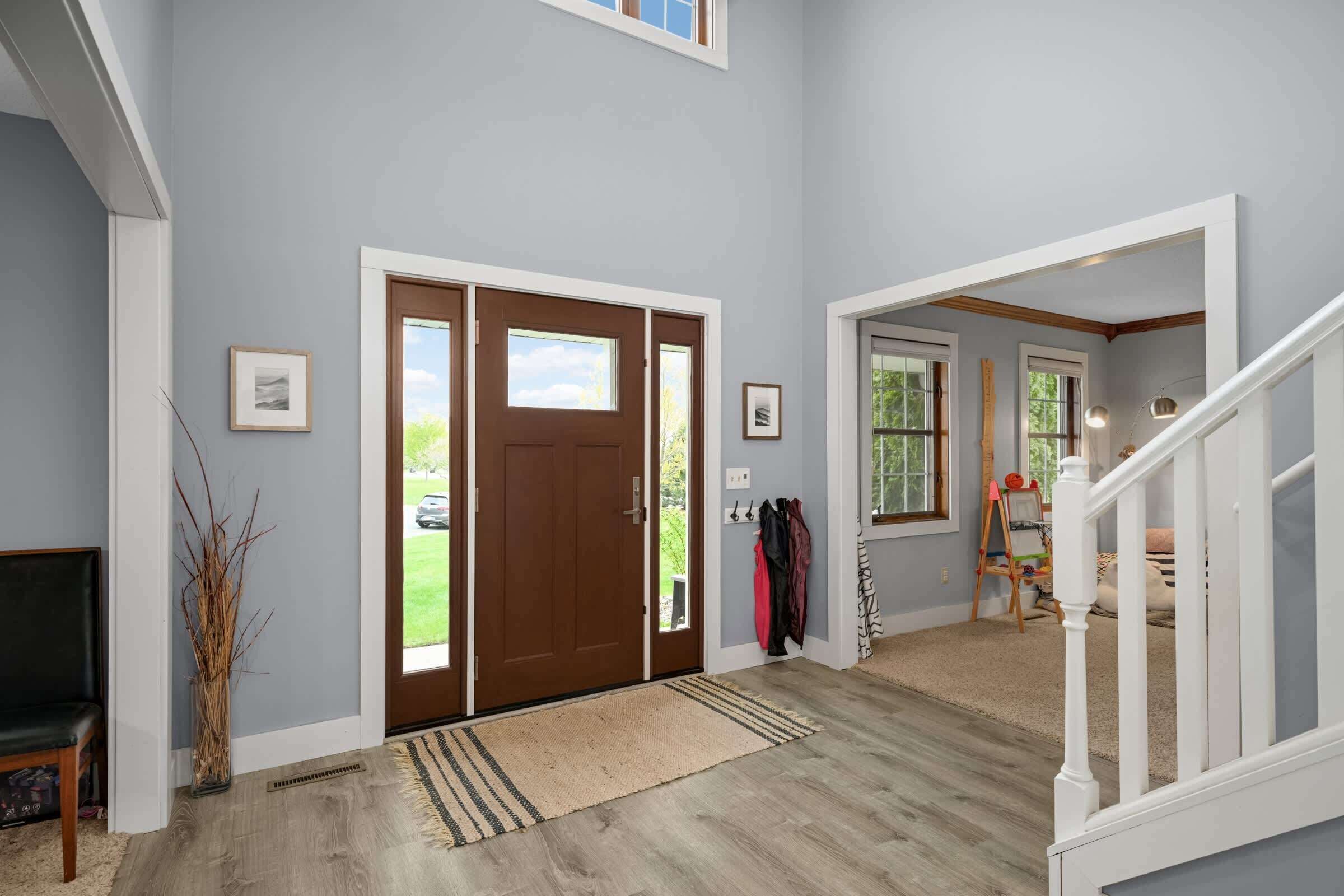A spacious entryway with a double door, a bench, a coat rack, and a staircase leading to another level.