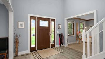 A spacious entryway with a double door, a bench, a coat rack, and a staircase leading to another level.