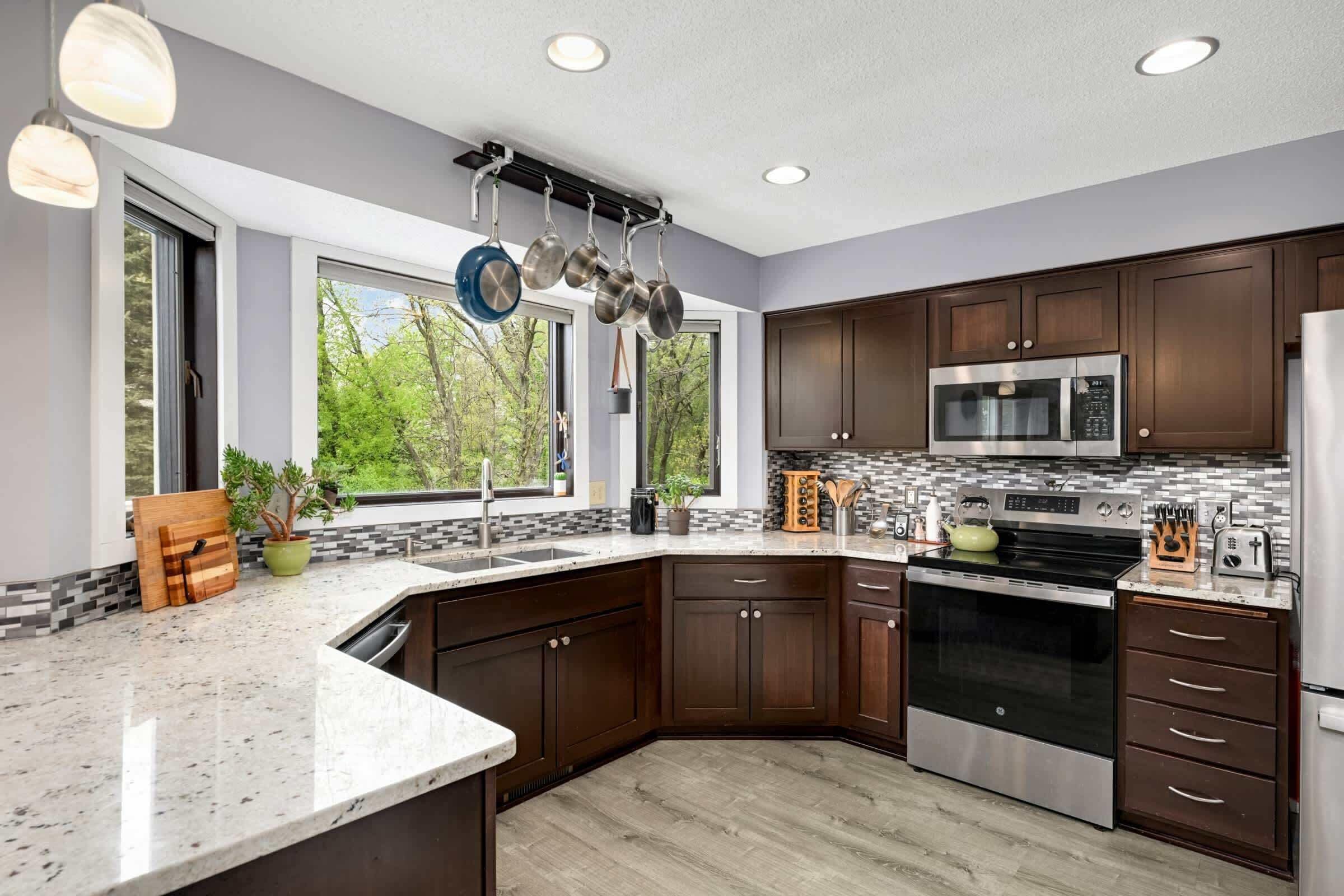 A modern kitchen with dark wood cabinets, stainless steel appliances, a granite countertop, and a hanging pot rack.