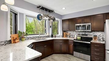 A modern kitchen with dark wood cabinets, stainless steel appliances, a granite countertop, and a hanging pot rack.