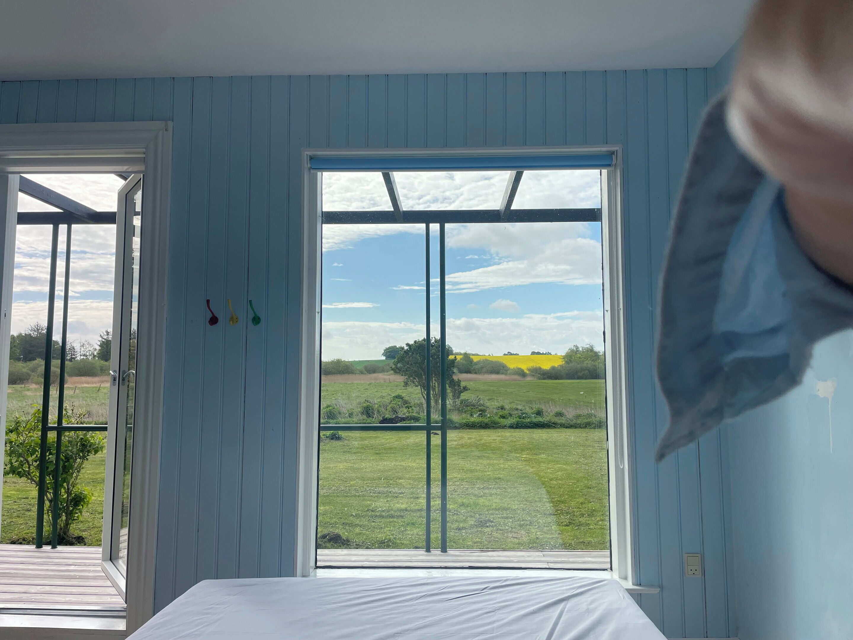A bedroom with a large window, a bed, and a door leading to an outdoor area.