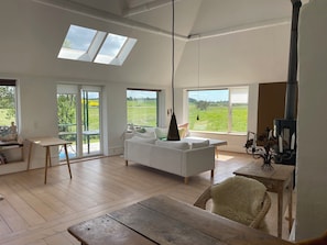 Een ruime woonkamer met een witte bank, een houten tafel en een open haard.
