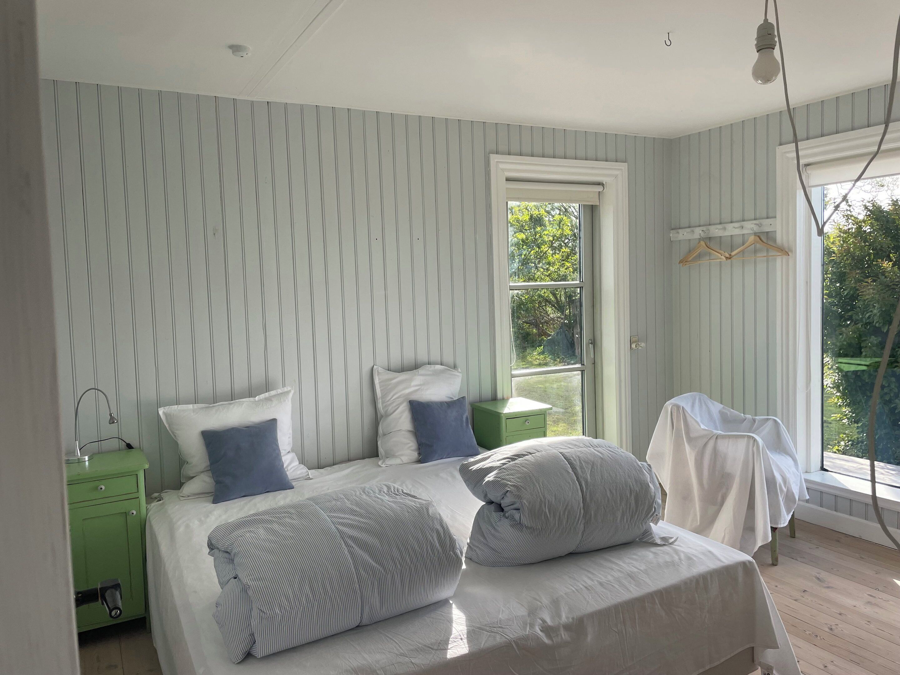 A bedroom with a bed, pillows, a bedside table, a window, and a hanging light fixture.