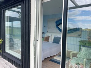 Een slaapkamer met een bed, kussens, een nachtkastje, een raam en een schilderij aan de muur.