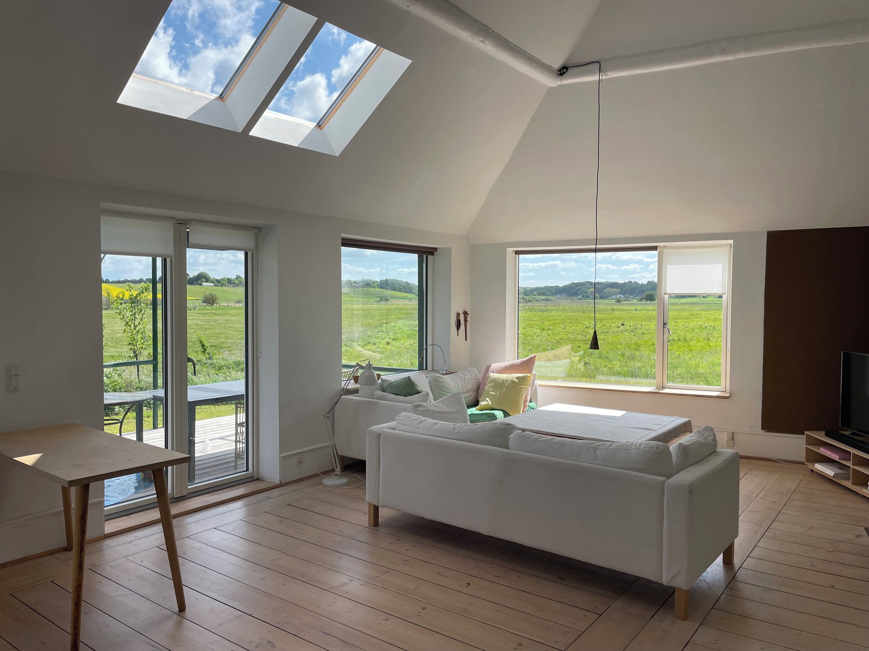 A spacious room with a large bed, a table, and multiple windows offering views of a green field.
