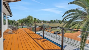 Een houten terras met een zwembad, tuinmeubilair en uitzicht op het omliggende landschap.