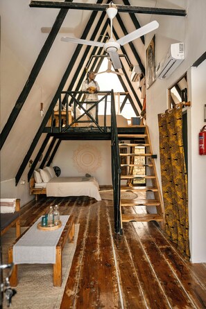 A loft-style room with a wooden staircase, a bed, a table with candles, and a ceiling fan.