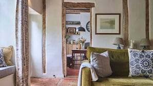 Una sala de estar acogedora con un sofá verde, cojines estampados, una zona de comedor con mesa de madera y un acceso rústico.