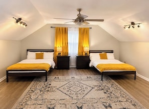 Une chambre avec deux lits, un ventilateur de plafond, un tapis à motifs et une fenêtre avec des rideaux.