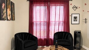 Una sala de estar con dos sillones negros, una mesa de centro redonda con un adorno decorativo, una cortina roja y un ventanal grande.