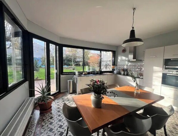 A modern kitchen with a central island, large windows, and a dining area with chairs.