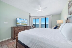 A hotel room with a large bed, a ceiling fan, a television, a view of the ocean, and a balcony with curtains. - Phoenix 10 Unit 1417 |  Next to Flora-Bama! | Beachfront | Pools | My Beach Getaways (Orange Beach)