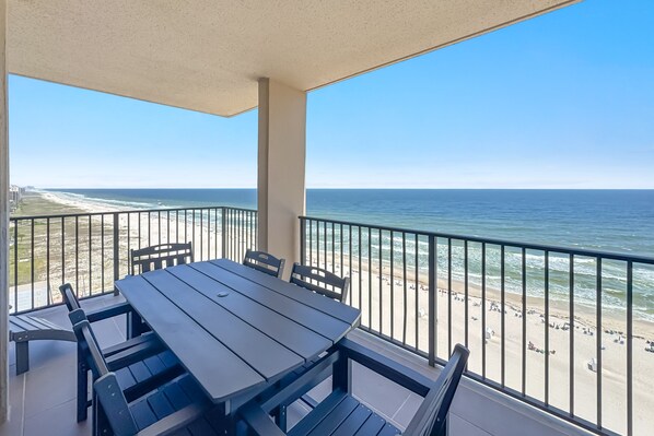A balcony with a table and chairs, overlooking a beach and ocean. - Phoenix 10 Unit 1417 |  Next to Flora-Bama! | Beachfront | Pools | My Beach Getaways (Orange Beach)